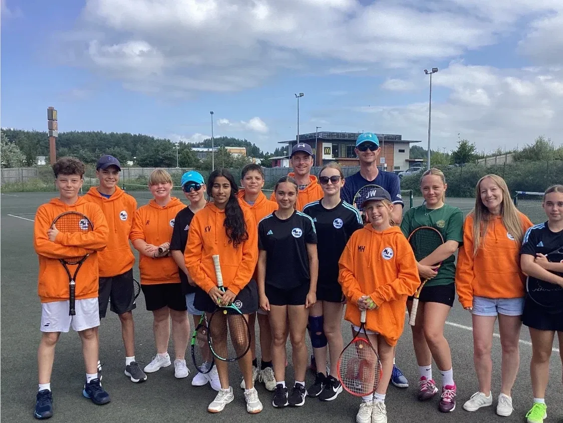MH Tennis juniors and coaches in team kit lined up together on court