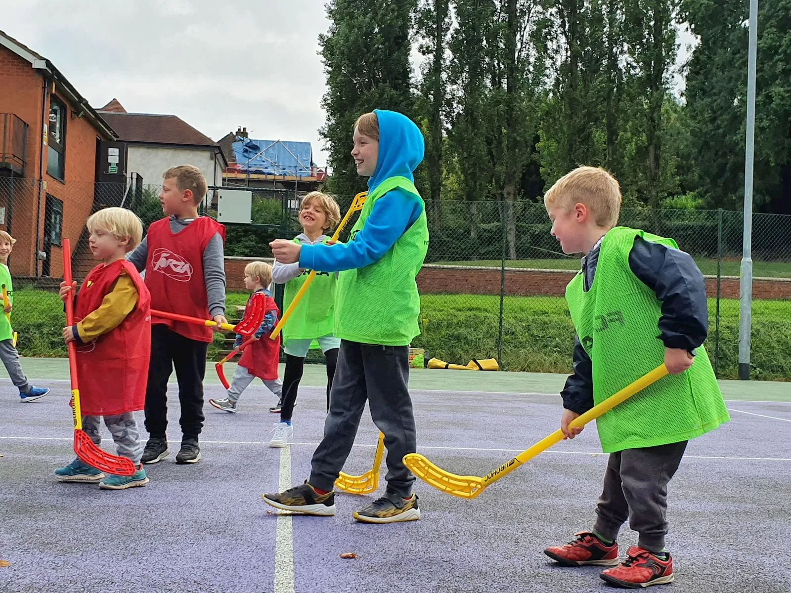 Young children in bibs playing hockey with plastic sticks at camp