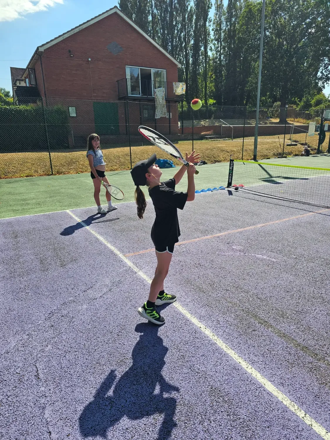 A young player tossing the ball up to serve on a sunny court