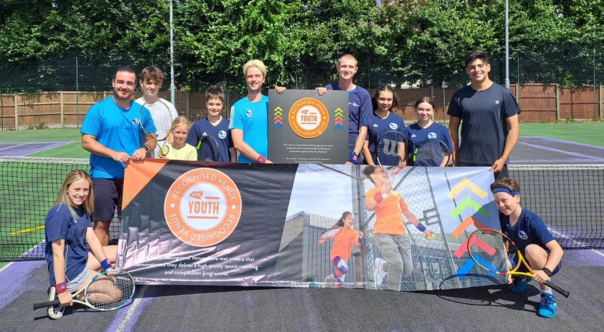 MH Tennis Young Leaders and coaches holding the LTA Youth Recognised Venue banner at the net